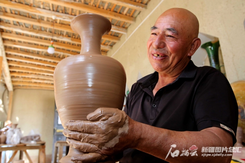 6月19日，英吉沙縣芒辛鎮(zhèn)恰克日庫依村土陶非遺傳承人阿卜杜熱合曼·麥麥提敏在欣賞剛制作的土陶作品。石榴云/新疆日?qǐng)?bào)記者 蔡增樂 攝